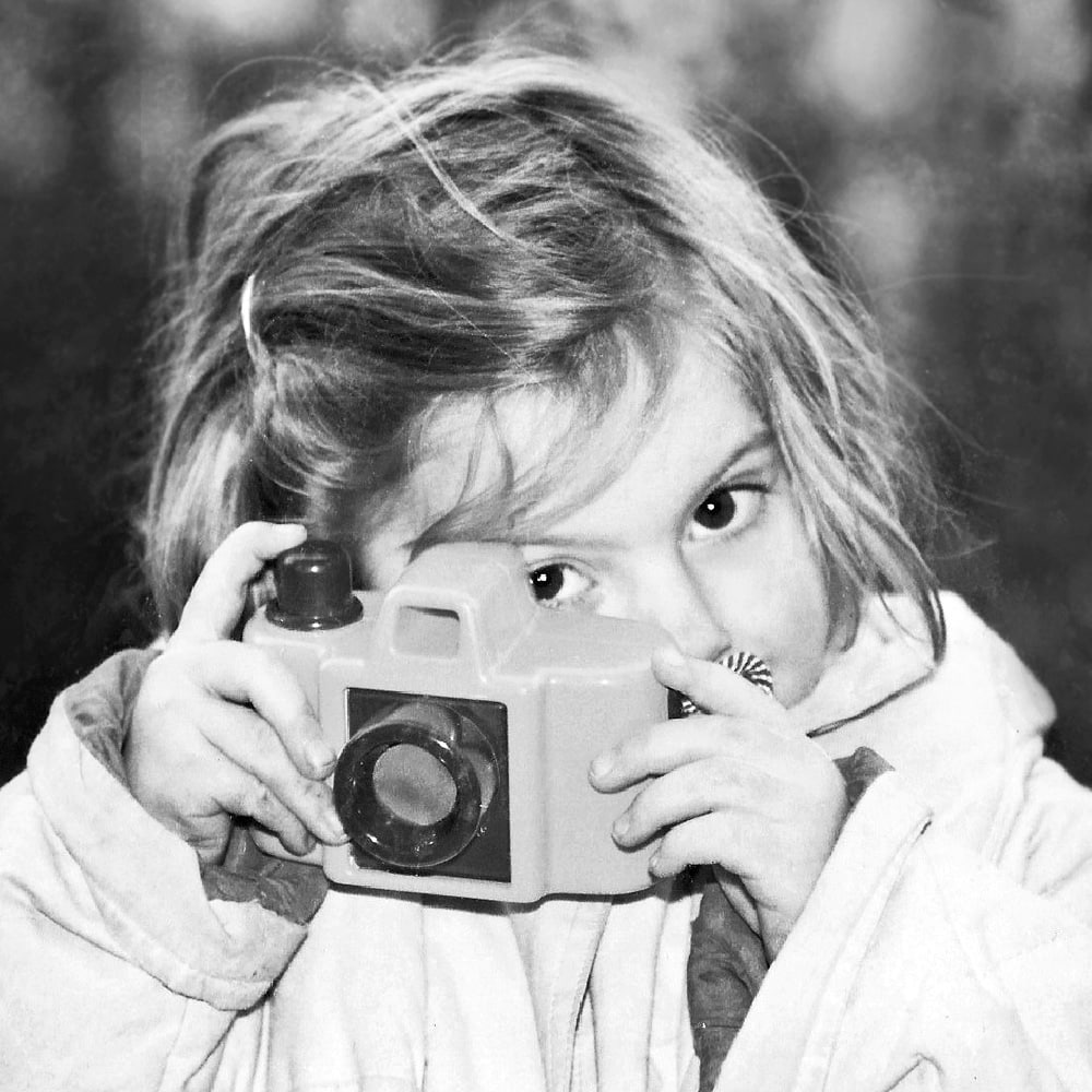 Photographer Marie Calfopoulos as a kid, holding a toy camera